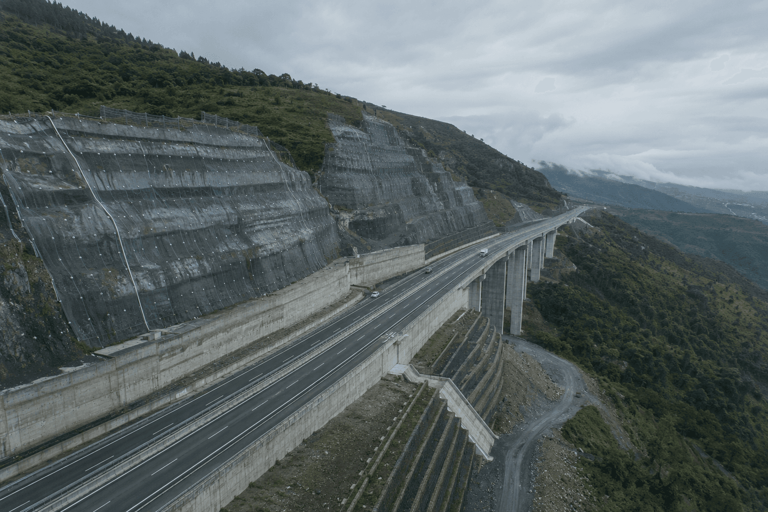 Highway viaduct beside a bolted and mesh-covered rock-cut slope.